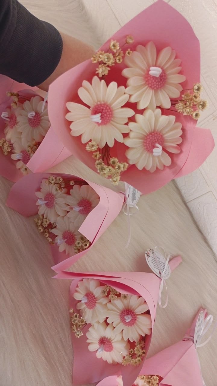 Ramos de velas en forma de margaritas blancas con centros rosados y envoltorio rosa.