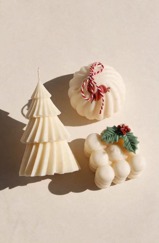 Tres velas navideñas claras: árbol geométrico y dos diseños redondeados con detalles festivos